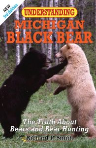 Two black bears, one with dark fur and one with light fur, stand on their hind legs facing each other in a grassy area. The book cover text reads "Understanding Michigan Black Bear," by Richard P. Smith.