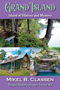 Book cover for "Grand Island: Island of History and Mystery" by Mikel B. Classen, featuring images of a forest bench, a lake with cliffs, a log cabin, and a rocky shoreline. The cover has a purple background.