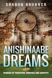 A book cover with a dreamcatcher decorated with beads and feathers hanging against a tree bark background. The title "Anishinaabe Dreams" and author "Sharon Brunner" are displayed in large text.