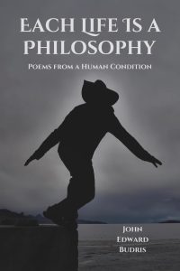 A silhouetted person in a hat balances on one foot against a cloudy sky. The book cover reads, “Each Life Is a Philosophy: Poems from a Human Condition” by John Edward Budris.